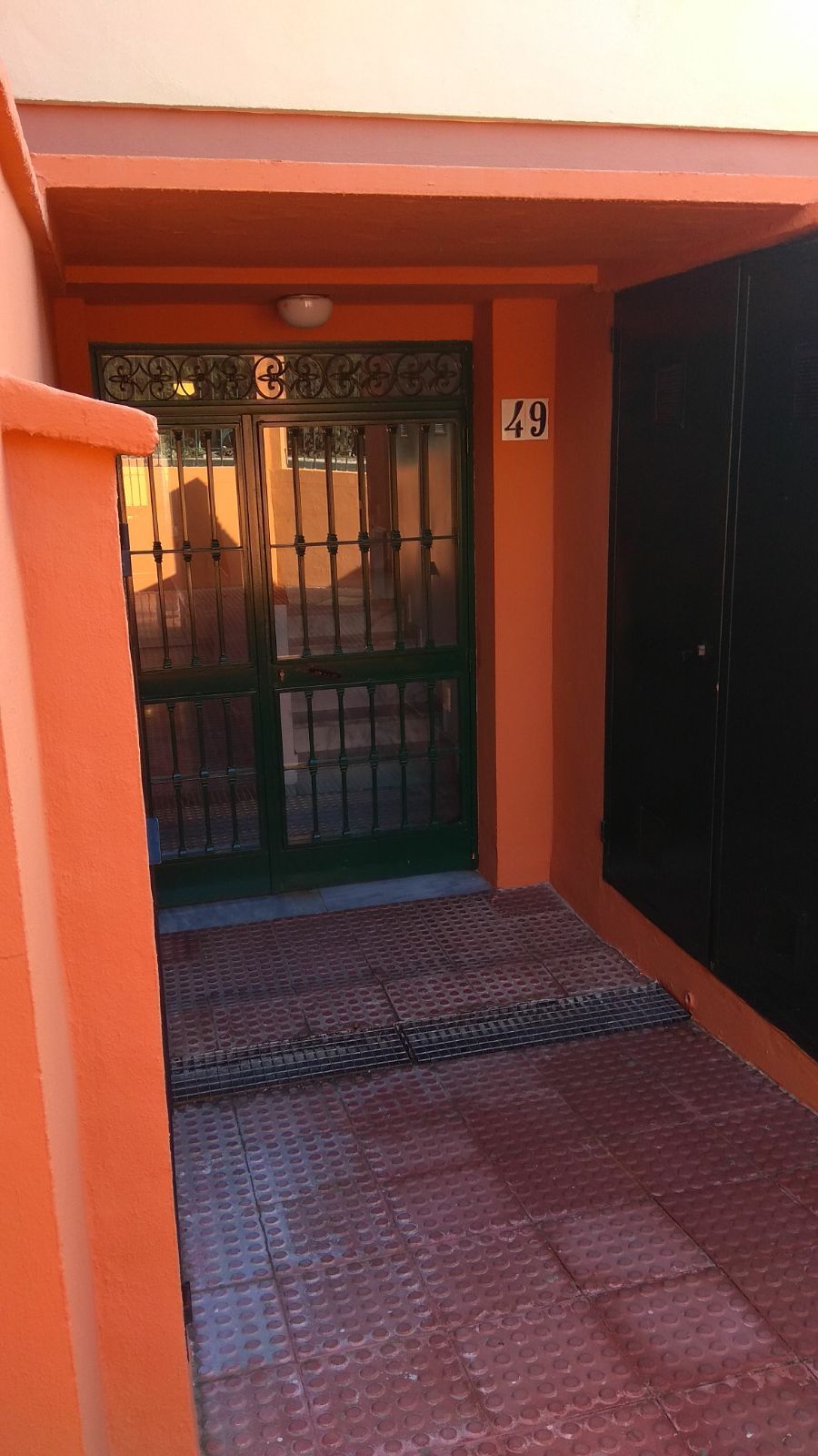 Entrada de un edificio con una verja metálica verde, el número 49 y una puerta negra.
