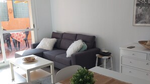 En stue med en grå sofa, et hvidt sofabord og et spisebord med en plante som midtpunkt.