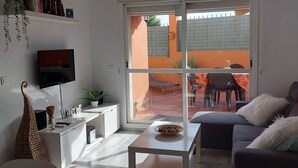 En moderne stue med sofa, sofabord og et fjernsyn monteret på væggen. Der er en skydedør, der fører ud til en udendørs patio.