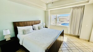Una camera d'albergo con un ampio letto, un comodino, una lampada e vista su una piscina.