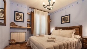 A bedroom with a large bed, a wooden headboard, a bedside table, a nightstand, a chandelier, and a window with curtains.