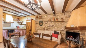 A rustic dining area with a wooden table and chairs, a stone fireplace, and a cozy seating area with a sofa and cushions.