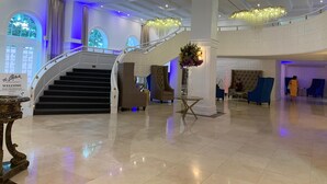 Eine großzügige Lobby mit einer imposanten Treppe, stilvollen Kronleuchtern und einem einladenden Schild.