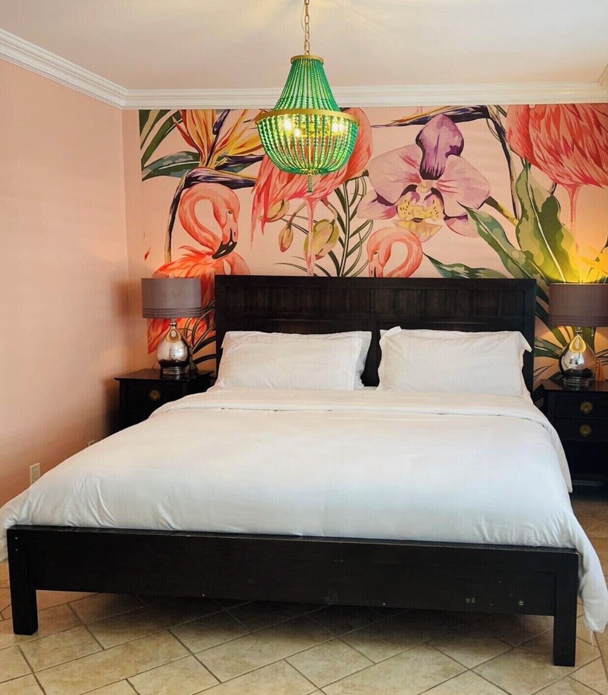 Ein Schlafzimmer mit Bett, zwei Nachttischen, einer hängenden grünen Leuchte und floralem Wandpapier.