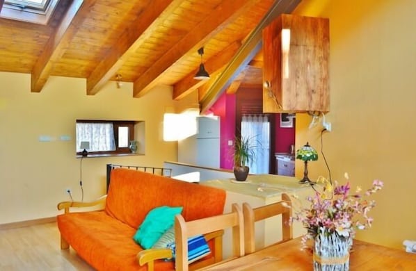A cozy living room with a wooden ceiling, a sofa, a dining table, and a vase of flowers.