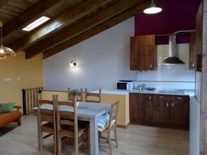 A cozy kitchen with wooden cabinets, a dining table with chairs, and a microwave.