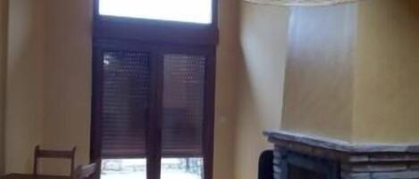 A dining area with a table and chairs, a fireplace, and a large window with blinds.