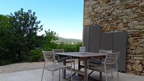 Une terrasse extérieure avec un mur en pierre, une table en bois et des chaises en métal.