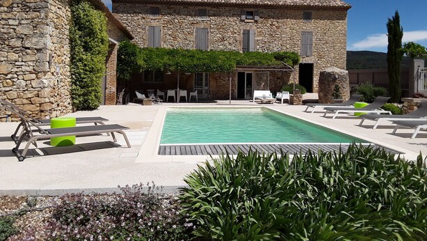 Un bâtiment en pierre doté d’une piscine, d’un espace extérieur aménagé et de verdure.