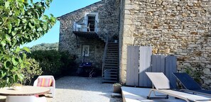 A stone building with a balcony, a staircase, outdoor seating, and a garden area.