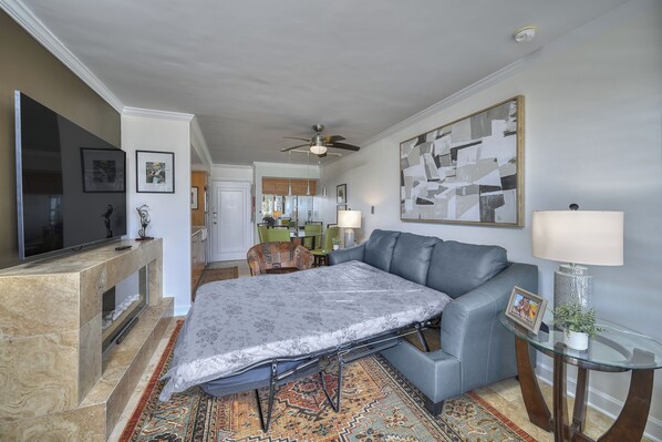 A living room with a sofa, a glass coffee table, a fireplace, and a television. - Savoy 203- Luxury 1BR- Spectacular Ocean View (MYRTLE BEACH)