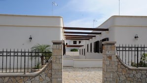 Una entrada protegida con muros de piedra y un camino empedrado que lleva a un edificio con una pérgola.