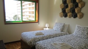 Ein Hotelzimmer mit zwei Betten, einem Fenster, einer Lampe und einem Wandbild.