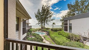 A view from a balcony overlooking a swimming pool, lush greenery, and a distant ocean view. - Sea Grape Inn #6- Beachfront Property (Longboat Key)