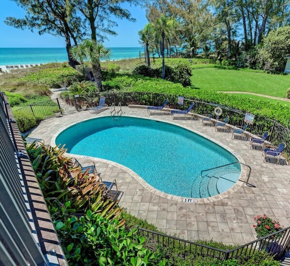 A swimming pool with a curved edge, surrounded by a paved deck and lounge chairs.