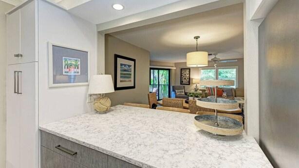 A modern kitchen with a marble countertop, built-in cabinets, and a seating area with a sofa and chairs. - Sea Grape Inn #6- Beachfront Property (Longboat Key)