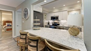 A modern kitchen with a marble countertop, stainless steel appliances, and a dining area with wooden chairs. - Sea Grape Inn #6- Beachfront Property (Longboat Key)