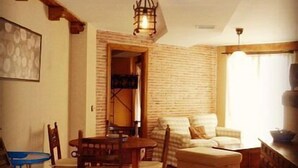 A cozy living room with a wooden dining table, chairs, a sofa, and a kitchen area with a counter.