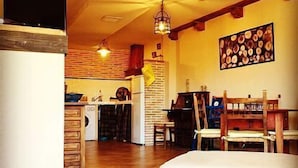 A cozy living room with a wooden coffee table, a dining area with a table and chairs, a kitchen with a brick wall, and a hanging light fixture.