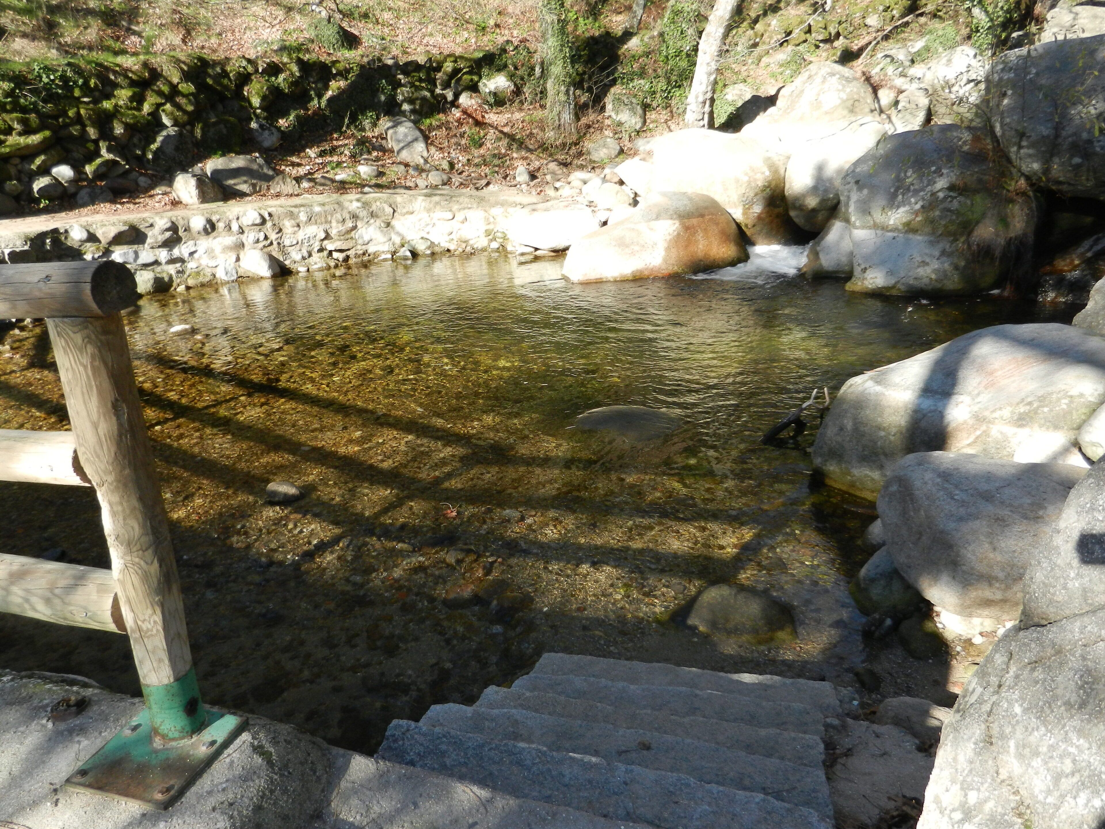 A stone staircase leading to a clear water body surrounded by rocks and greenery.