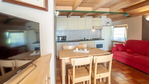 A compact kitchen with wooden cabinets, a dining table, and a red sofa. - Chalet Terme Bormio - REIT (Bormio)