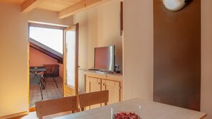 A wooden dining table with chairs, a television on a cabinet, and a window with a view of the outside. - Chalet Terme Bormio - REIT (Bormio)