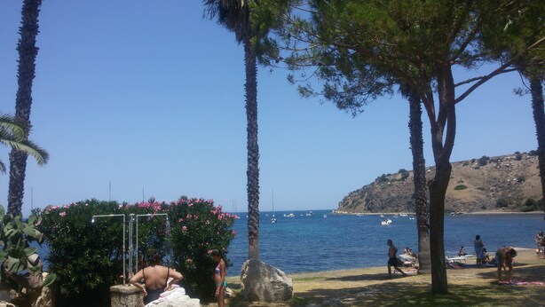 Una playa con palmeras, un promontorio rocoso y barcos en el agua.