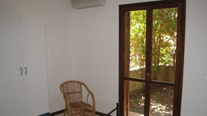 Una habitación con un ventanal grande, una silla de mimbre y una cama con colcha.