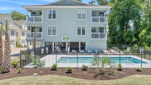 A two-story building with a pool, surrounded by a fence and palm trees. - Summer Times #4 - 2 Bedroom Located Close To The Beach (NORTH MYRTLE BEACH)