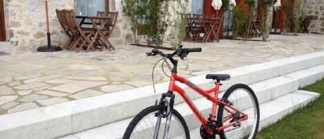 A red bicycle parked on outdoor steps in front of a building with stone walls and outdoor seating.