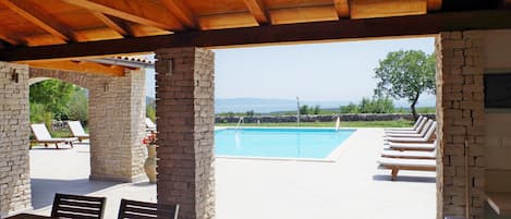 A covered outdoor area with a pool, lounge chairs, and a table.
