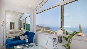 A modern living room with a blue sofa, a glass coffee table, and a view of the sea. - Dion Villa (Zakynthos Island)