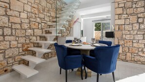 A modern dining area with a stone wall, a glass staircase, and blue chairs. - Dion Villa (Zakynthos Island)