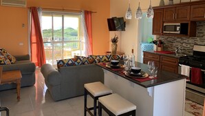 A modern kitchen with a central island, wooden cabinets, and a dining area with a sofa and chairs. - Paradise beach front condo with stunning views. (Flexible cancellations) (Antigua and Barbuda)