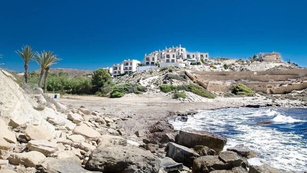 Un edificio costiero con diversi piani, situato su un pendio roccioso sotto un cielo azzurro.