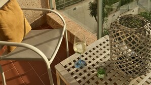 Un balcone con una sedia, un tavolo con un bicchiere di vino e vista sul mare e sul verde.