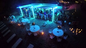 Un'area per eventi all'aperto con tavoli e sedie rotonde, illuminata da luci blu.