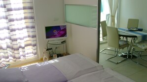 A hotel room with a bed, a desk with a chair, a television, and a window with curtains.