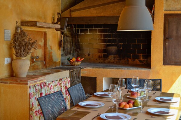 Un comedor con chimenea de ladrillo, una mesa para dos personas con platos, vasos y fruta.