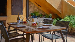 Un área de comedor al aire libre con una mesa preparada para cuatro personas, rodeada de sillas de mimbre.