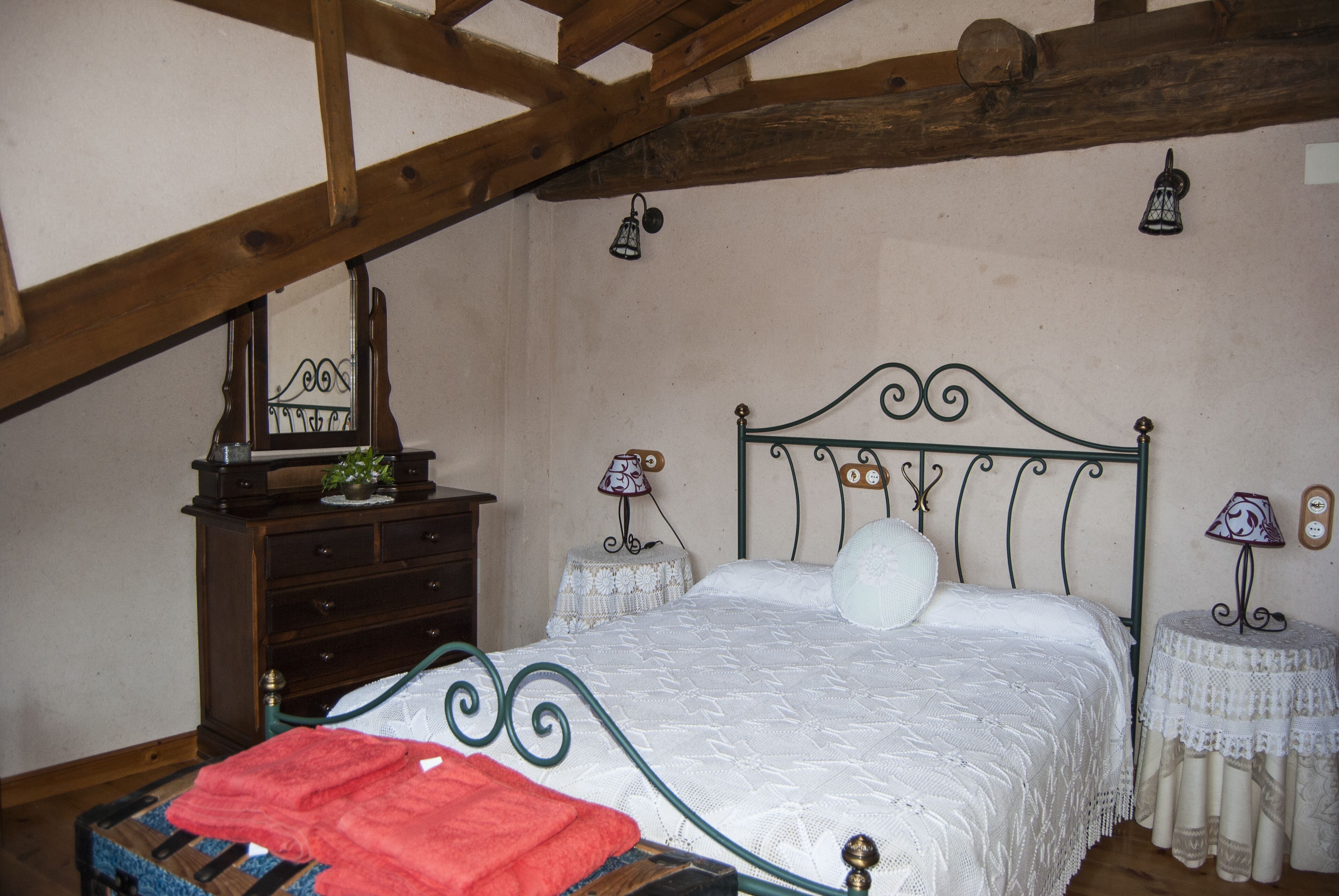 A bedroom with a bed, wooden beams, a dresser, and two bedside tables with lamps.