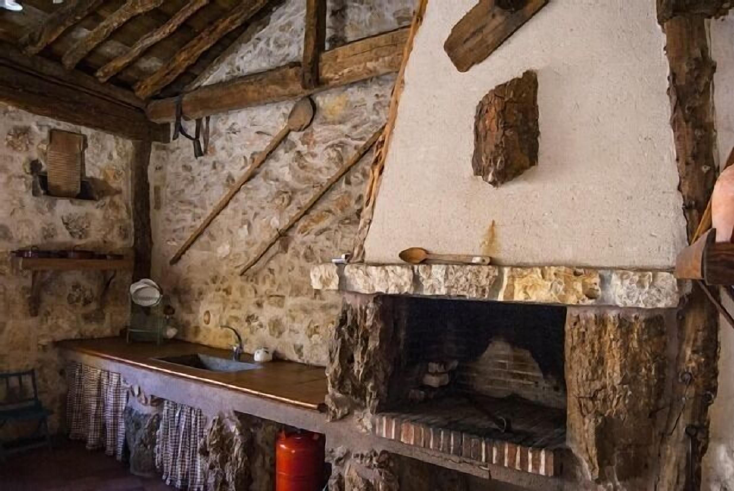 Una cocina rústica de piedra con chimenea de piedra, vigas de madera y un sencillo mostrador de madera.