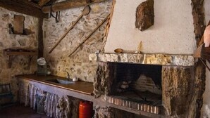 Tunnelmallinen, maalaishenkinen keittiö, jossa on kivitakka, puupalkit ja yksinkertainen puinen työtaso.