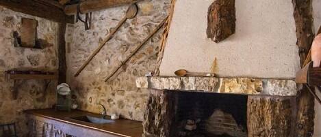 Una cocina rústica de piedra con chimenea de piedra, vigas de madera y un sencillo mostrador de madera.