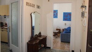 A hallway with a wooden console table, a mirror, and a door leading to a living room with a blue sofa and artwork on the wall. -  Sunflower Levanto central 100 meters from the sea with views across the valley (Levanto)