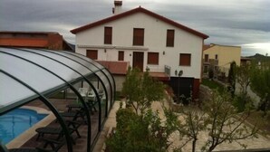 Une maison à deux étages avec un toit rouge et des murs blancs, une piscine et une serre.