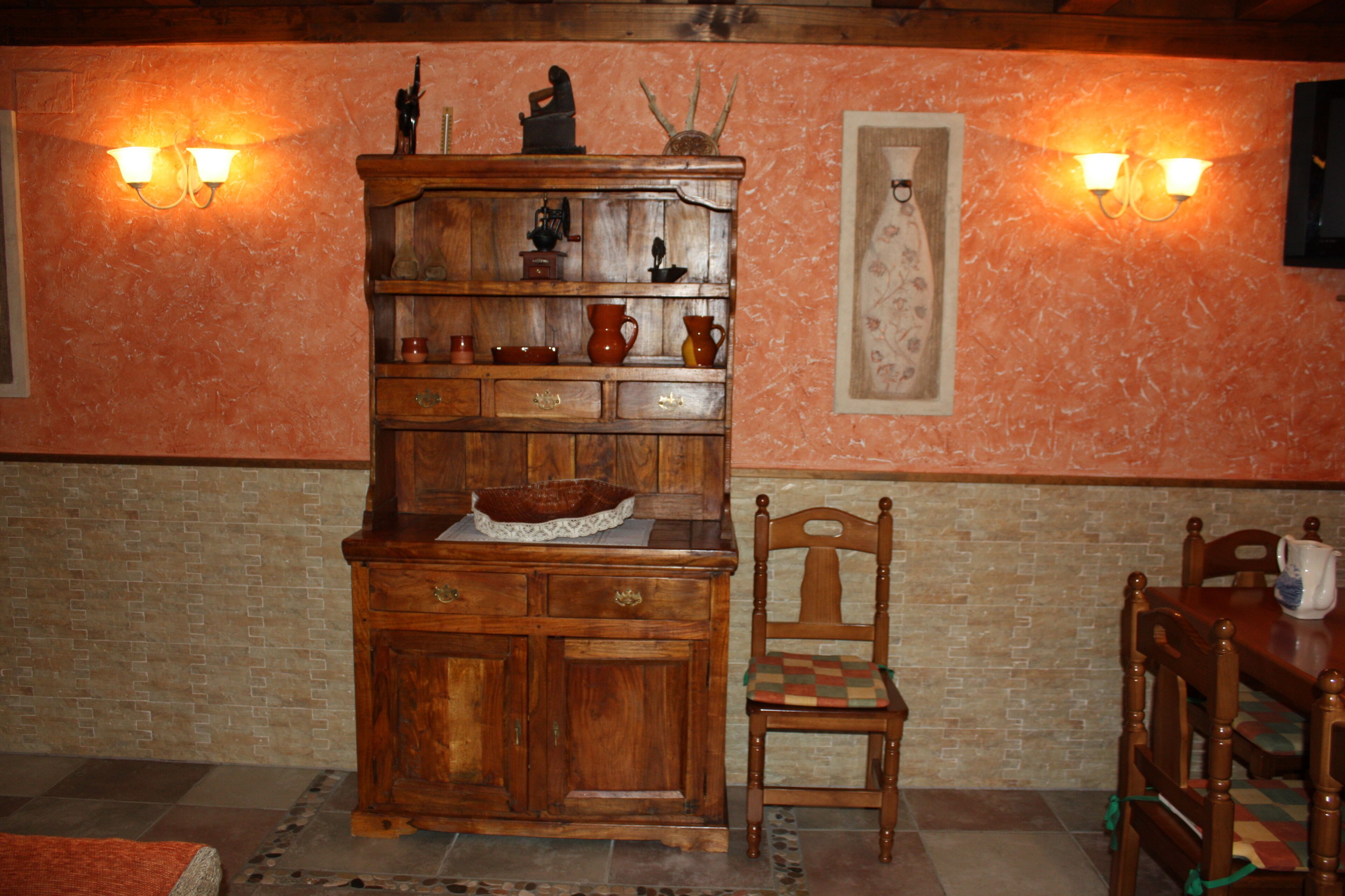 Een houten kast met lades en planken, een stoel met een geruit kussen, en een tafel met een kan.