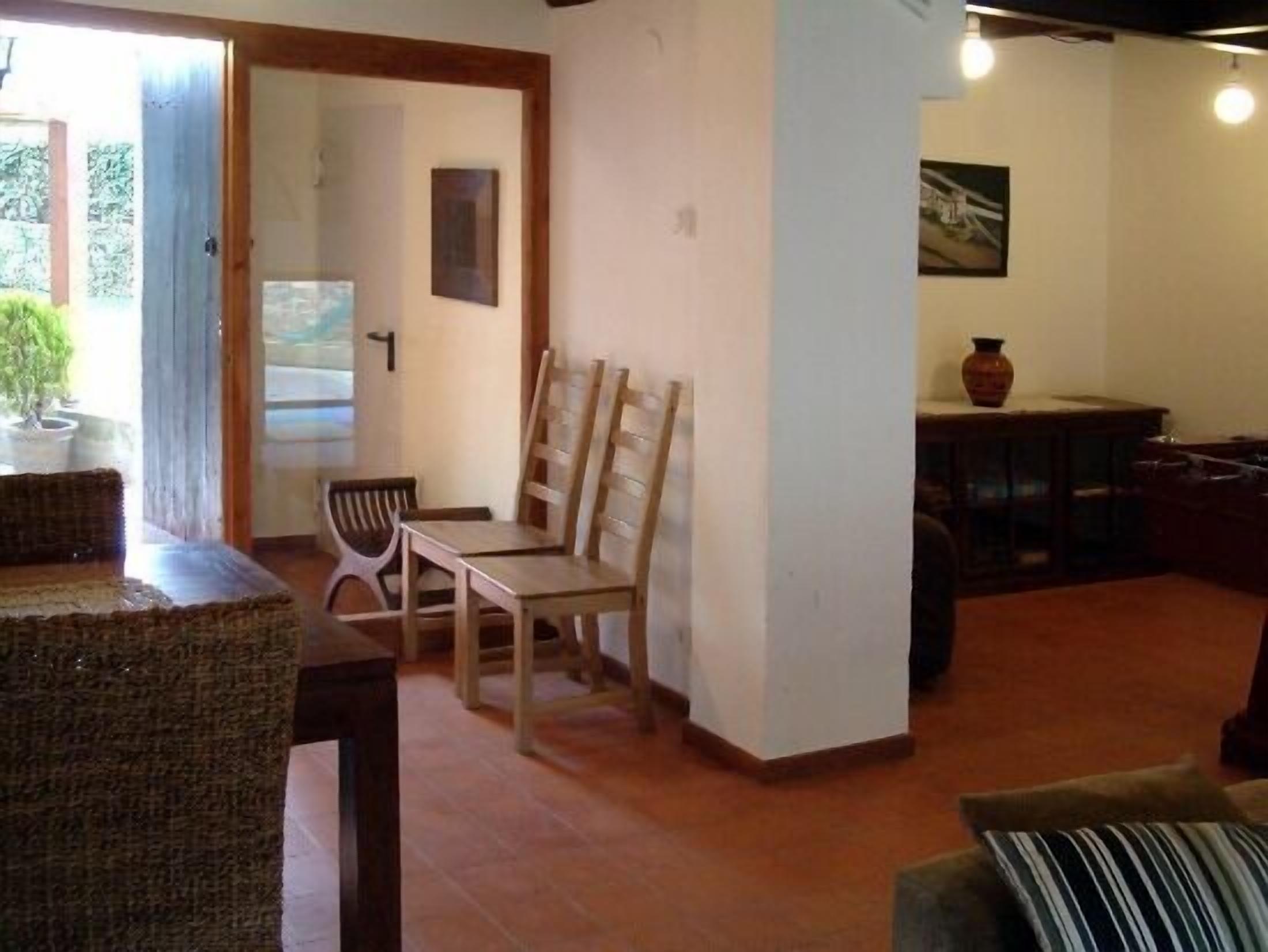 A cozy living room with a wooden coffee table, two wooden chairs, a sofa, and a small table with a vase.