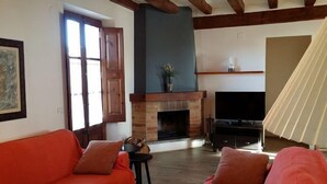 Ein Wohnzimmer mit Kamin, einer Couch, einem Fernseher und einem Fenster mit Vorhängen.