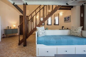 Une chambre avec un escalier en bois, un lit recouvert d’une couverture bleue, une table de chevet et une armoire verte.